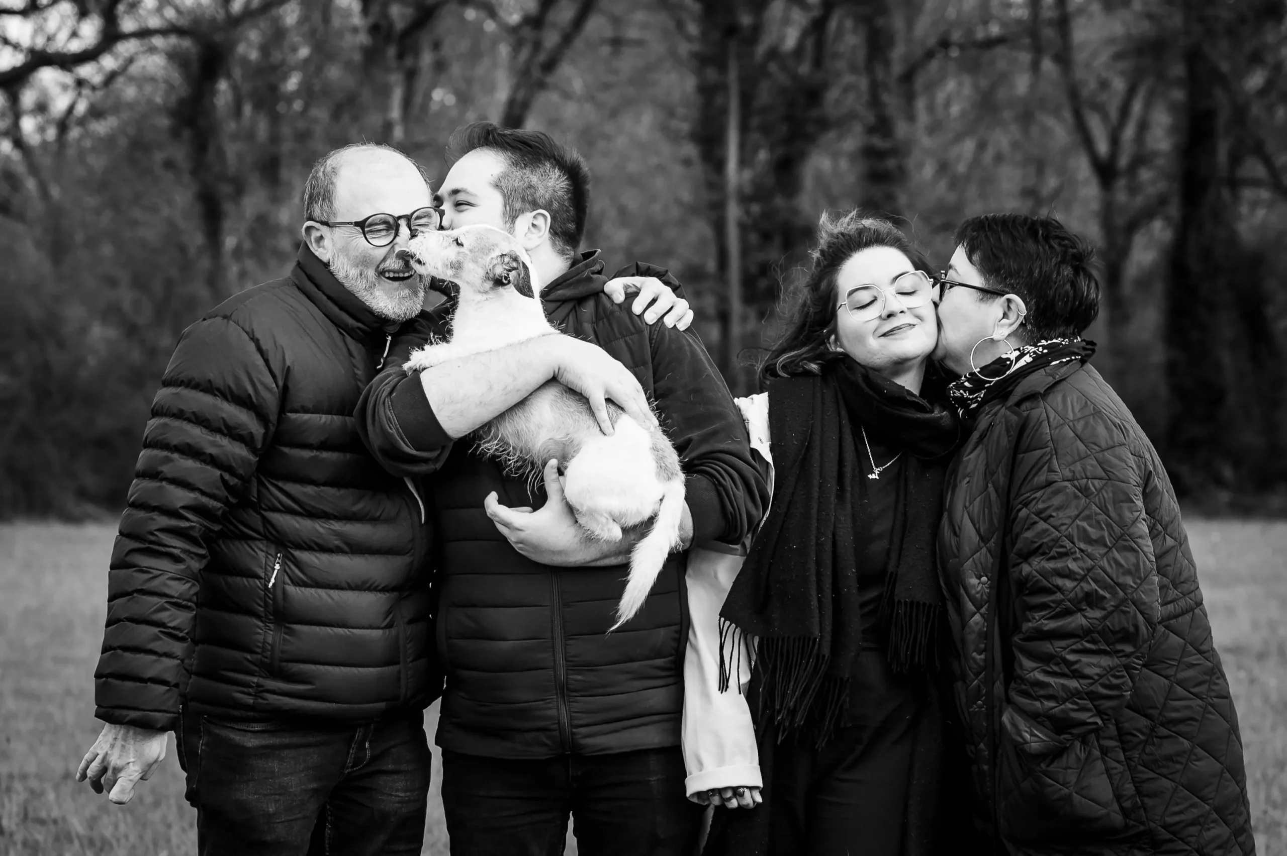 photo de famille, le chien lèche le nez de son maître, le fils embrasse son père et la maman embrasse sa fille