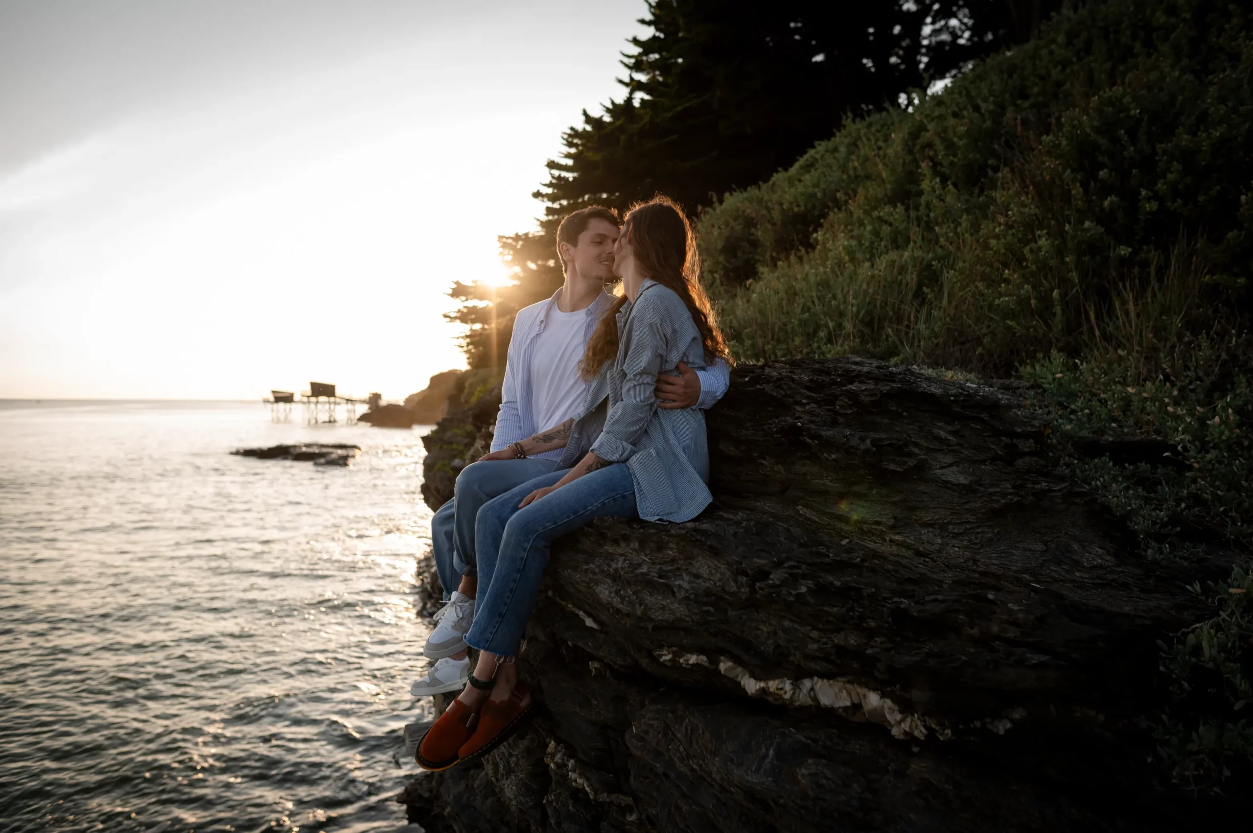 photo d’un couple assis sur un rocher face à la mer, coucher du soleil