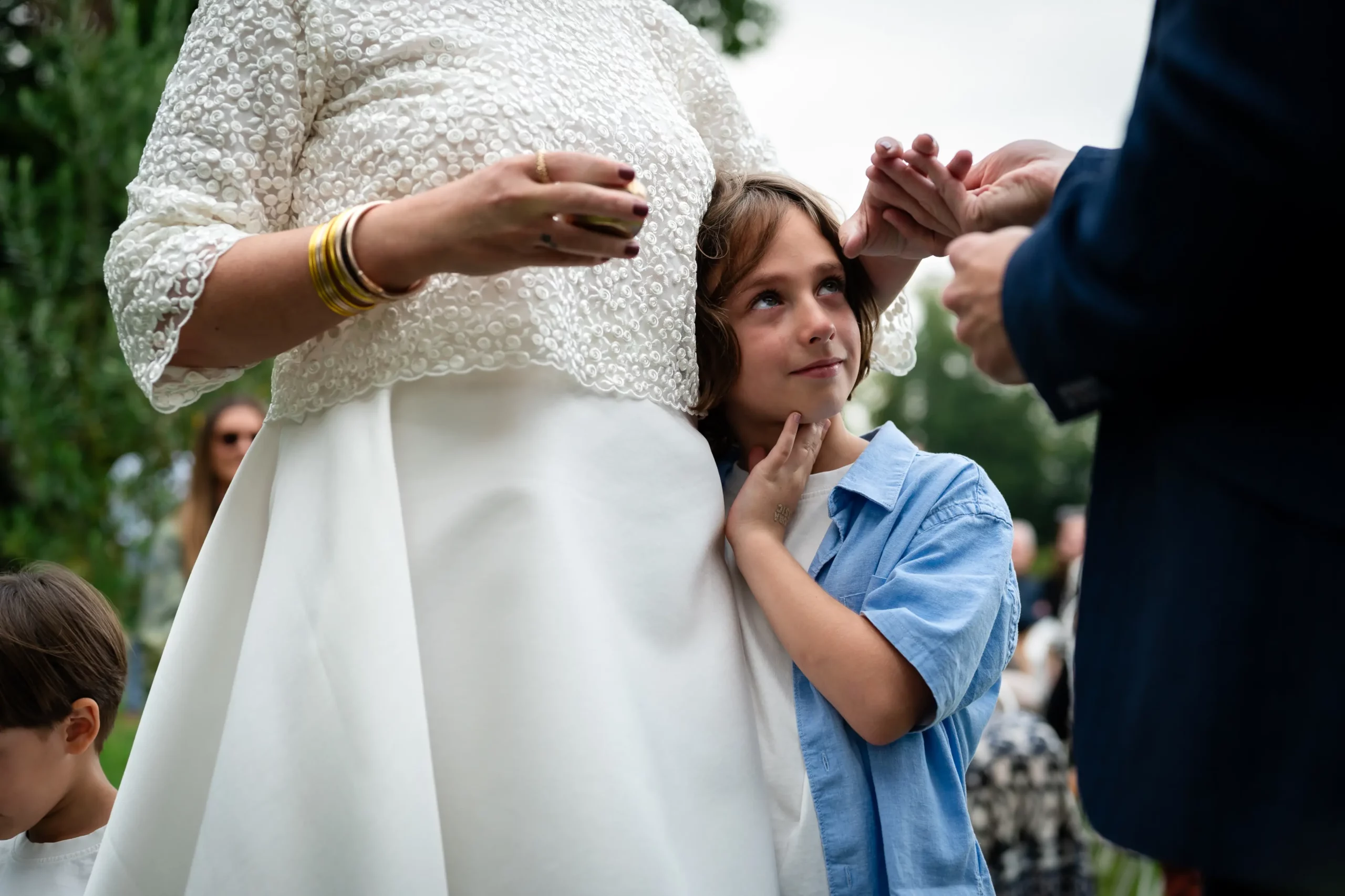 ceremonie-mariage-loire-atlantique reportage documentaire de mariage en loire atlantique. la scène se passe pendant le passage des alliances. le fils des mariée tient fort sa maman part la taille tout en regardant son papa mettre l'alliance au doigt de sa maman. le fils est très ému, on devine une larme qui coule sur sa joue