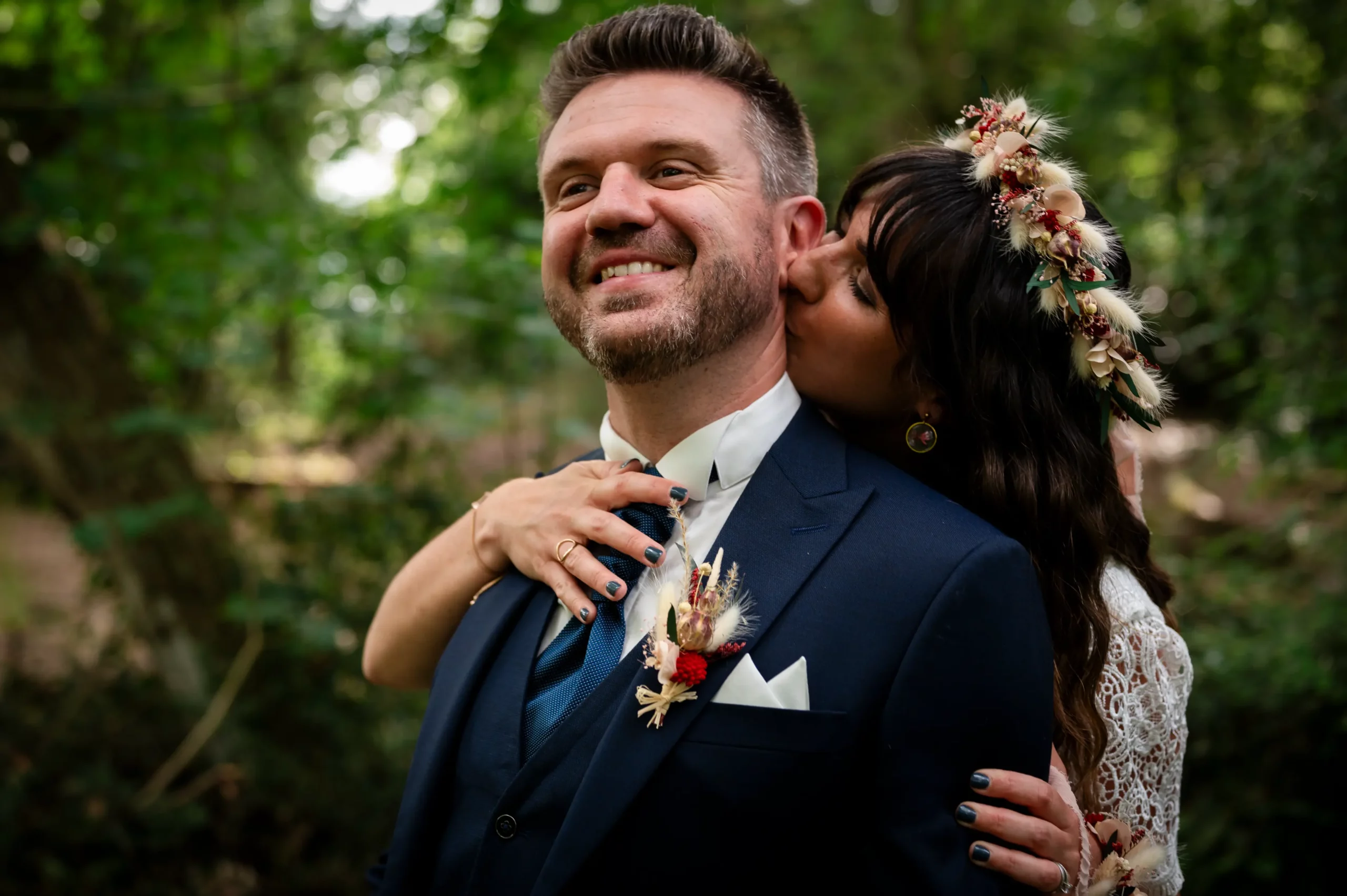 photographie de couple lors d'un mariage en Pays de la Loire, la mariée embrasse le marié dans le cou, le marié sourit