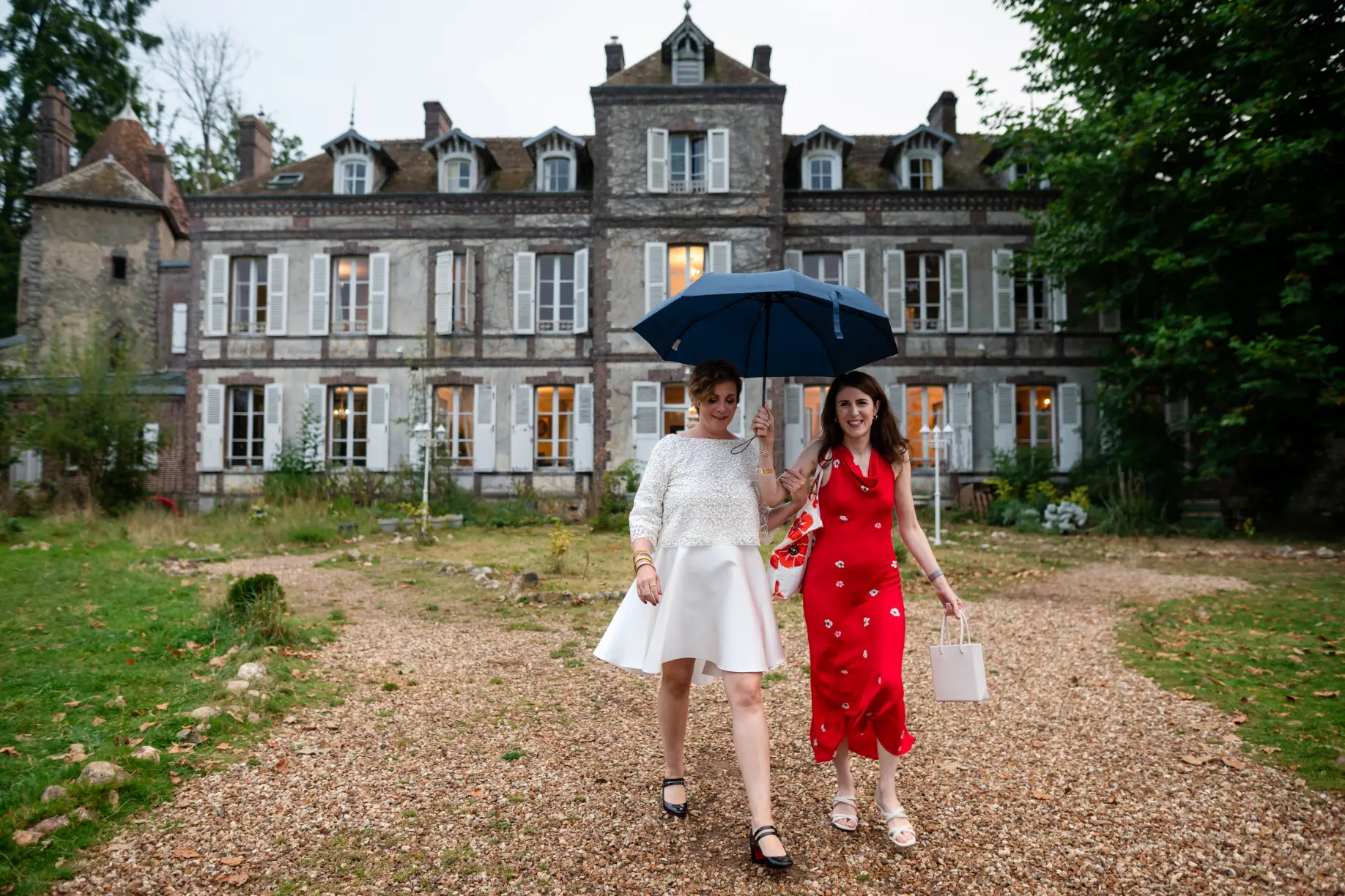 mariage-chateau-loire-atlantique photo de mariage originale, la scène se passedevant un chatêau de Loire Atlantique, la mariée et sa témoin portent un parapluie, en fond on voit la château