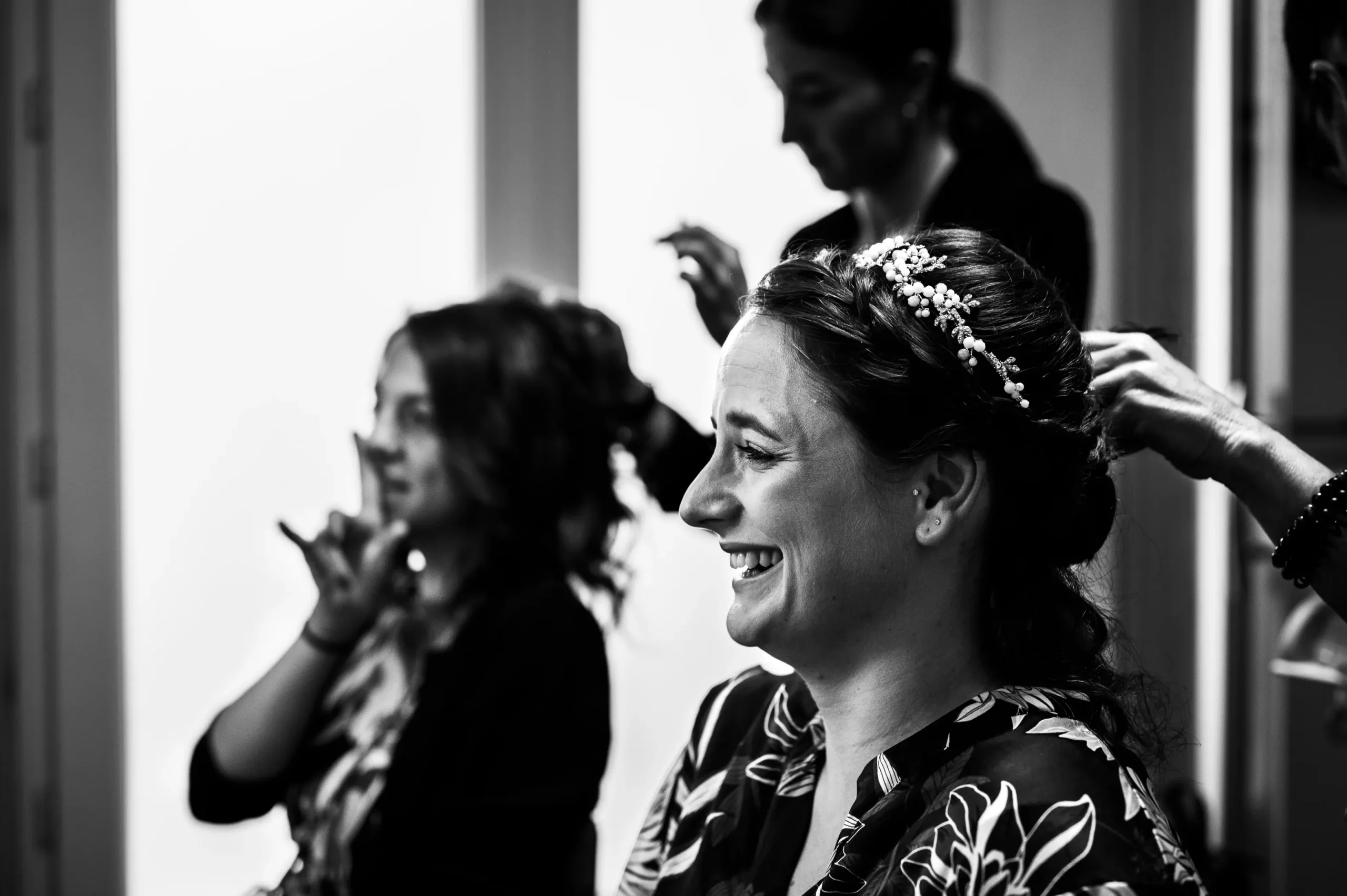 preparatif-mariage-angers-nb reportage photo de mariage à Angers, au domicile des parents de la mariée qui est en train d'être coiffée avec une coiffeuse professionnelle, en compagnie de sa témoin, toutes les deux rigolent. cette photo est en noir et blanc