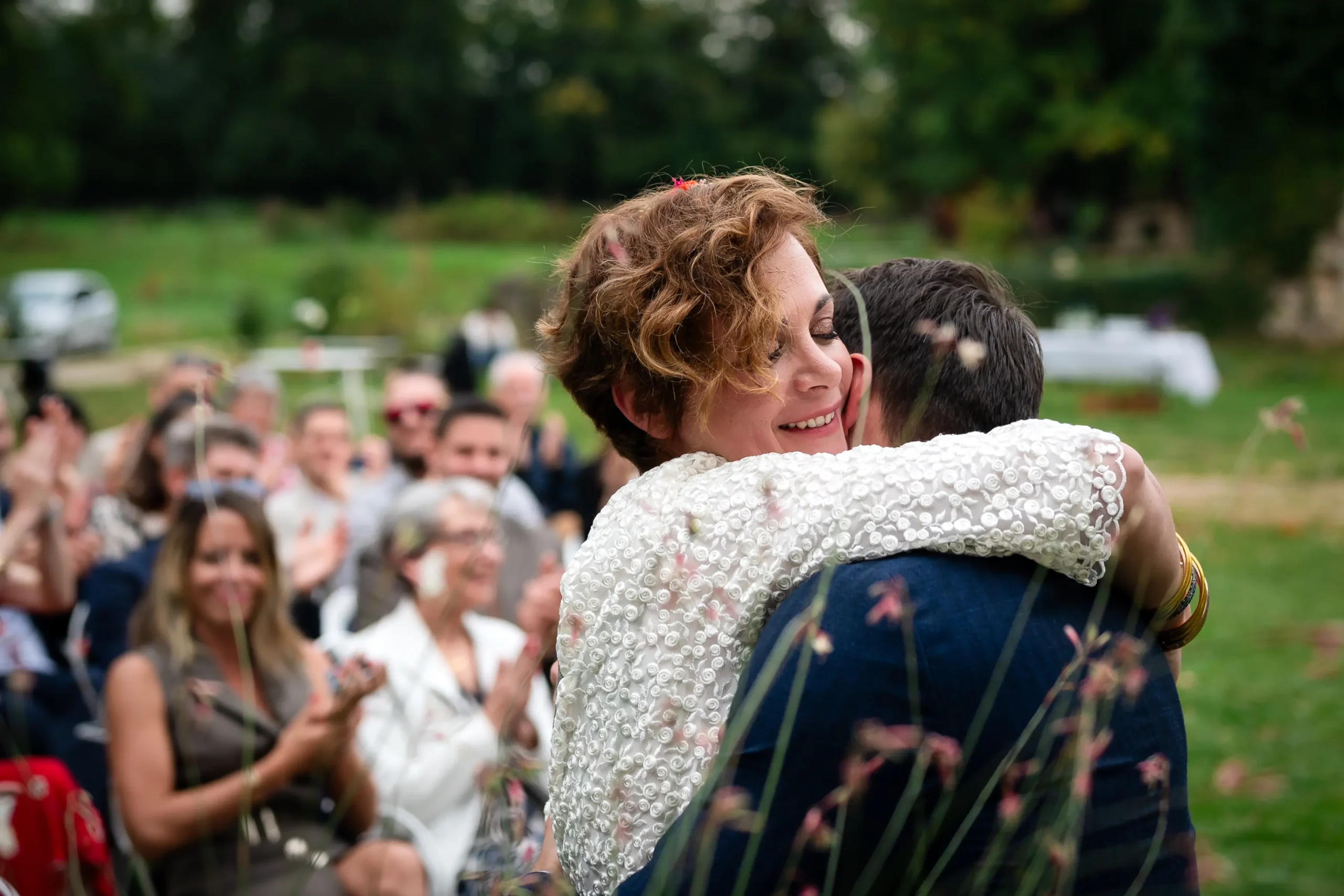 reportage-mariage-nantes photographie prise à la fin de la cérémonie laïque de mariage. la mariée prend dans ses bras le mariée avec en fond les invités qui les applaudissent