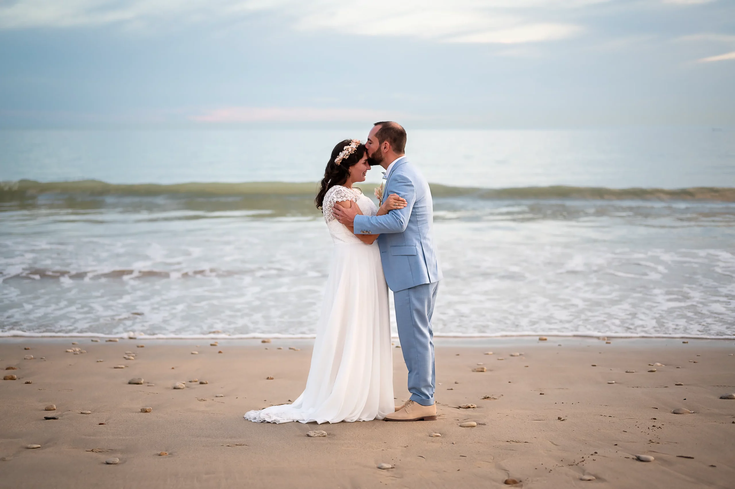 reportage-photo-mariag-ile-de-re-seance-couple-face-mer photographie prise sur l'ile de ré, d'un couple en premier plan avec la mer en second plan et une jolie vague. le marié embrasse le front de la mariée